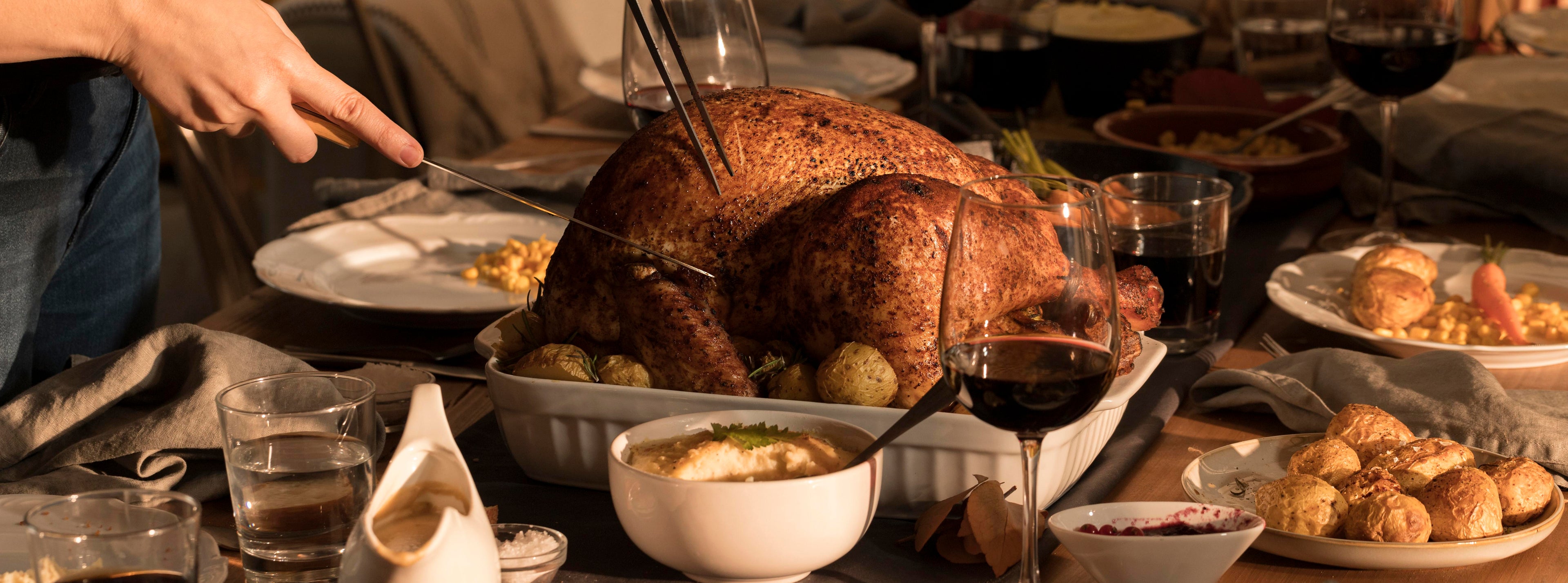 Person carving a turkey at a festive dinner table with wine glasses and side dishes.